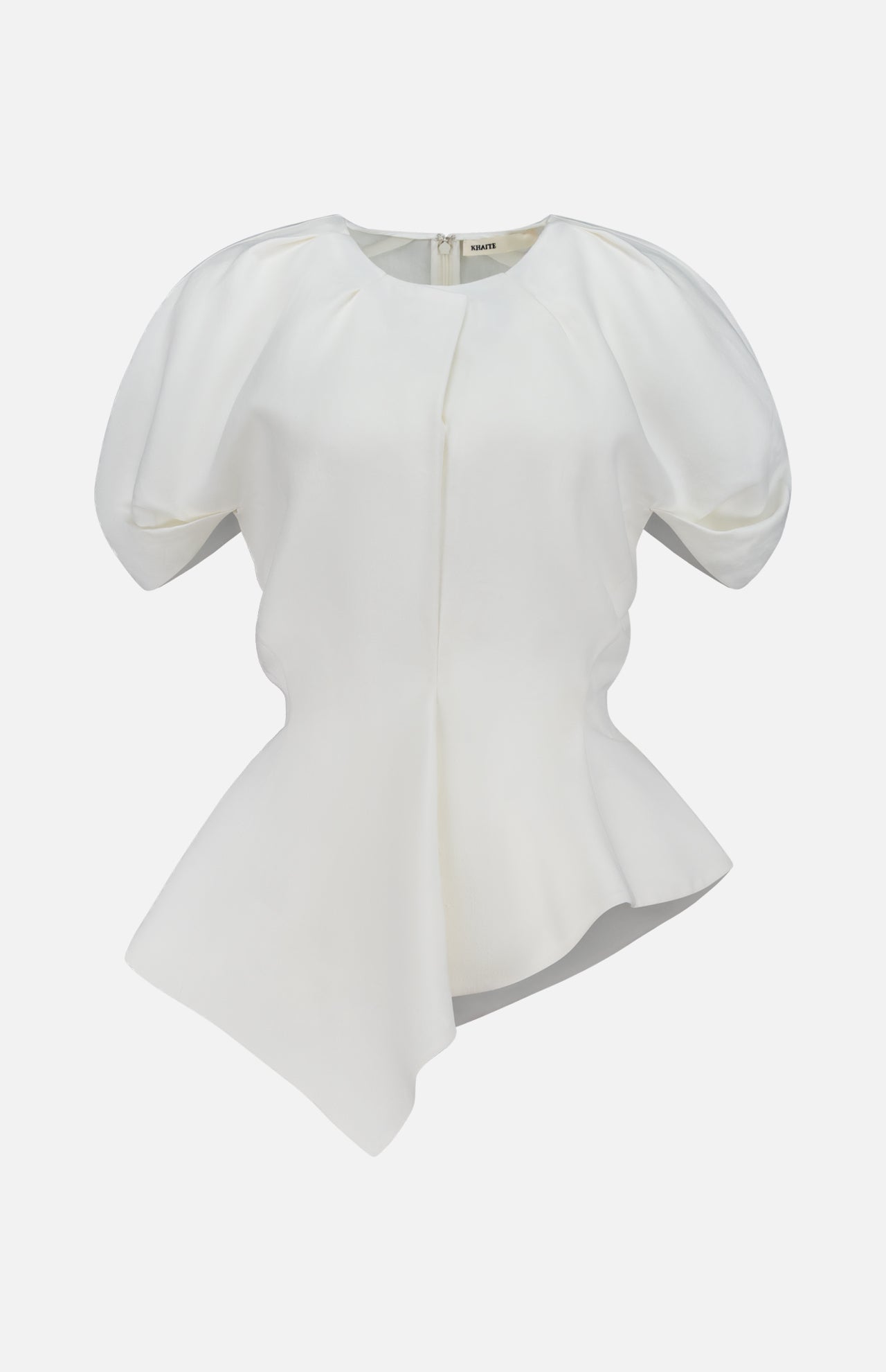 The Rumi Asymmetric Hem Top by KHAITE is a white short-sleeve blouse featuring puffed shoulders, a fitted waist, and an asymmetric hem. Crafted from a luxurious linen-viscose-silk blend, this draped top is displayed on a plain white background.
