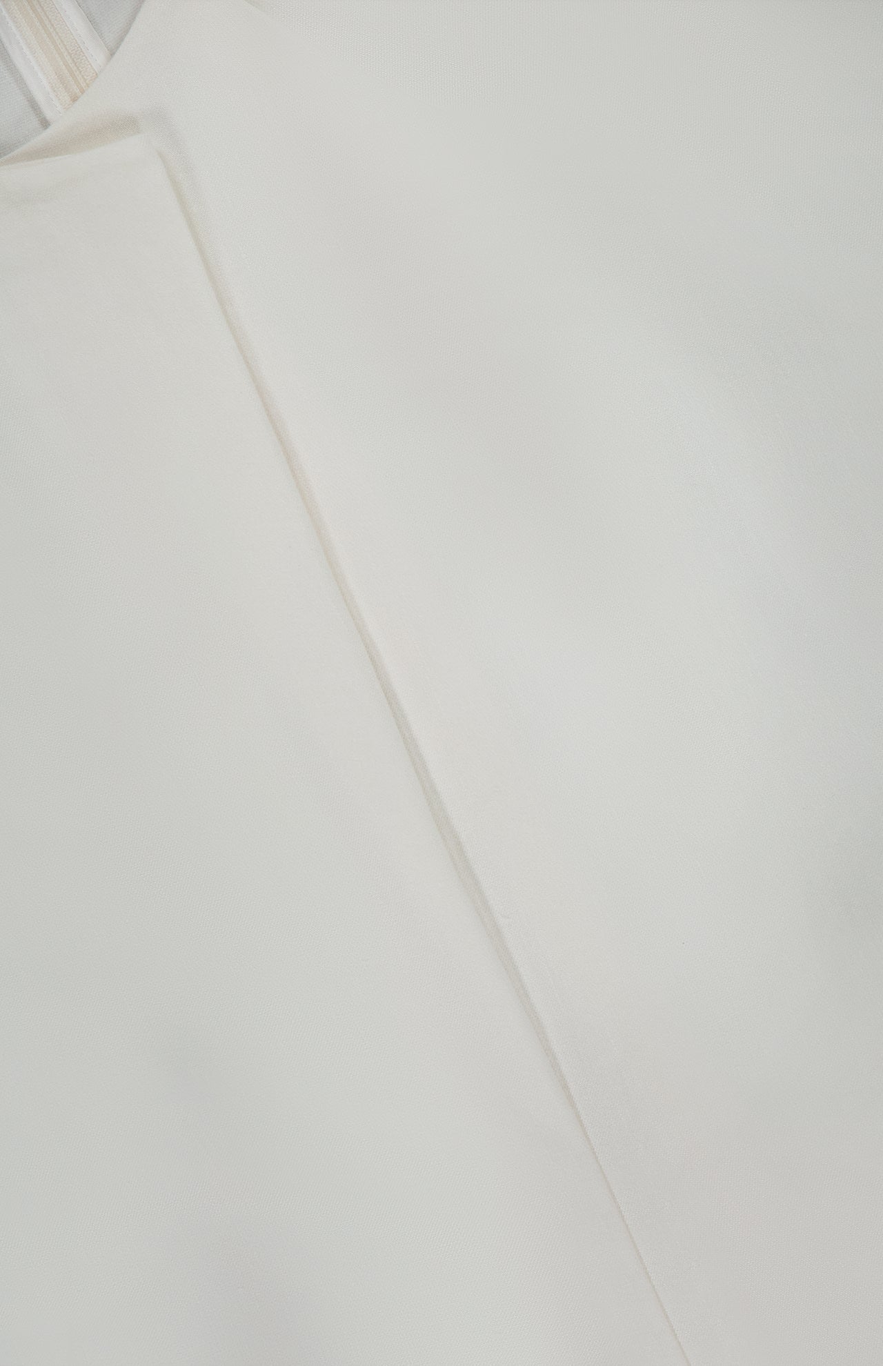 A close-up of the KHAITE Rumi Asymmetric Hem Top showcases its smooth white linen viscose silk fabric, featuring a distinctive diagonal seam that creates subtle shadows and highlights the refined texture.