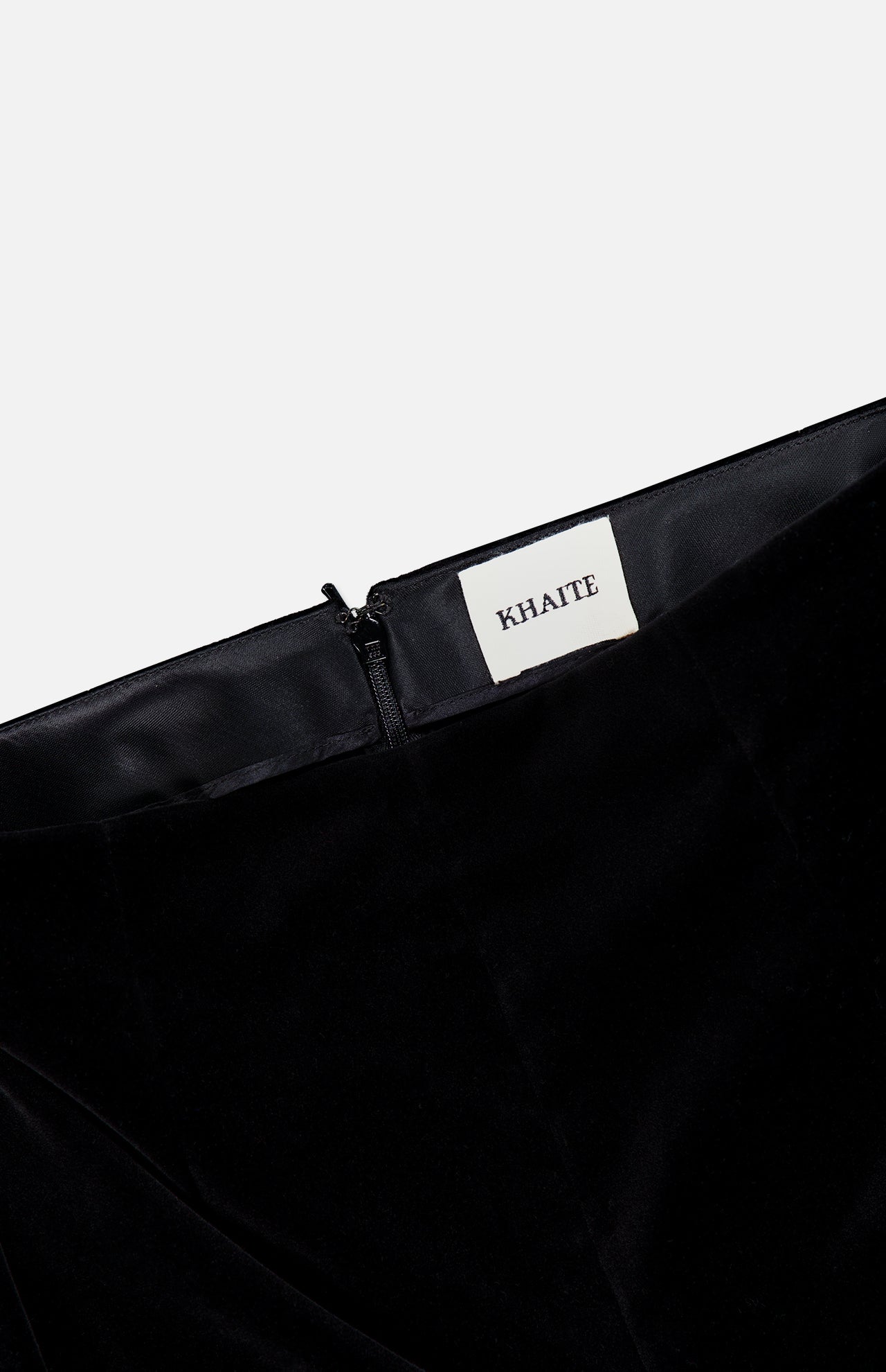 Close-up of the waistband on the Ryden Velvet Pant by KHAITE, showcasing a visible zipper and a white fabric label with the brand name stitched inside. The high-rise silhouette and lush velvet texture highlight its Italian craftsmanship.