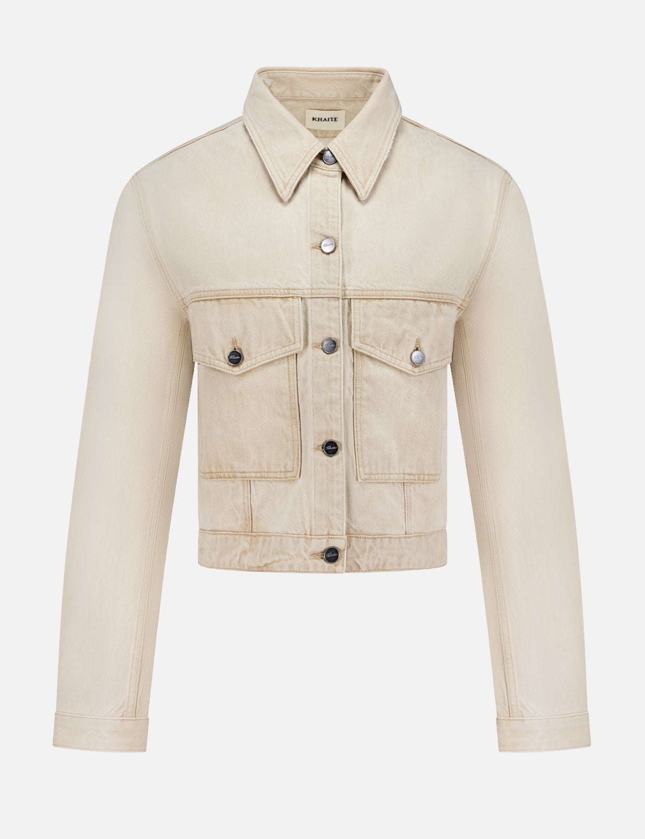 The Tomer Collared Cropped Denim Jacket by KHAITE features beige denim, a pointed collar, button-down front, long sleeves, and two chest flap pockets—perfect for a minimalist wardrobe. Shown on a white background.