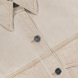 Close-up of the Tomer Collared Cropped Denim Jacket by KHAITE in beige denim, featuring black buttons and two front pockets. A white label inside the collar displays the brand name KHAITE—ideal for a minimalist wardrobe.