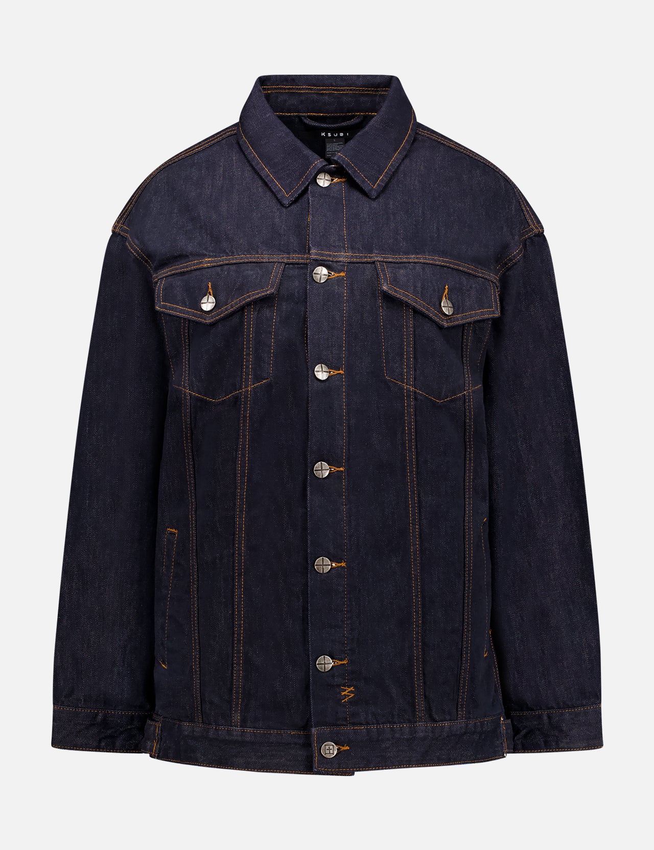 The KSUBI Longline Trucker Jacket features a dark indigo wash, silver buttons, front button closure, chest flap pockets with button details, contrast stitching, a classic collar, and a structured, slightly loose fit.