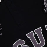Close-up of the KSUBI Duke Rugby Long Sleeve Jersey Shirt: black with a white collar and button, featuring large gray and white embroidered collegiate-style lettering, a crest patch, and smaller decorative text on this oversized top.