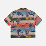 The KSUBI Mauna Loa Short Sleeve Diner Shirt features an oversized fit, vibrant tropical print with palm trees and mountains in blue, pink, yellow, and orange on a light background. Shown laid flat from the back.