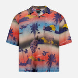 The KSUBI Mauna Loa Short Sleeve Diner Shirt is an oversized cotton modal shirt with a vivid tropical print of palm trees, mountains, and oceans in bold red, blue, yellow, and purple hues.