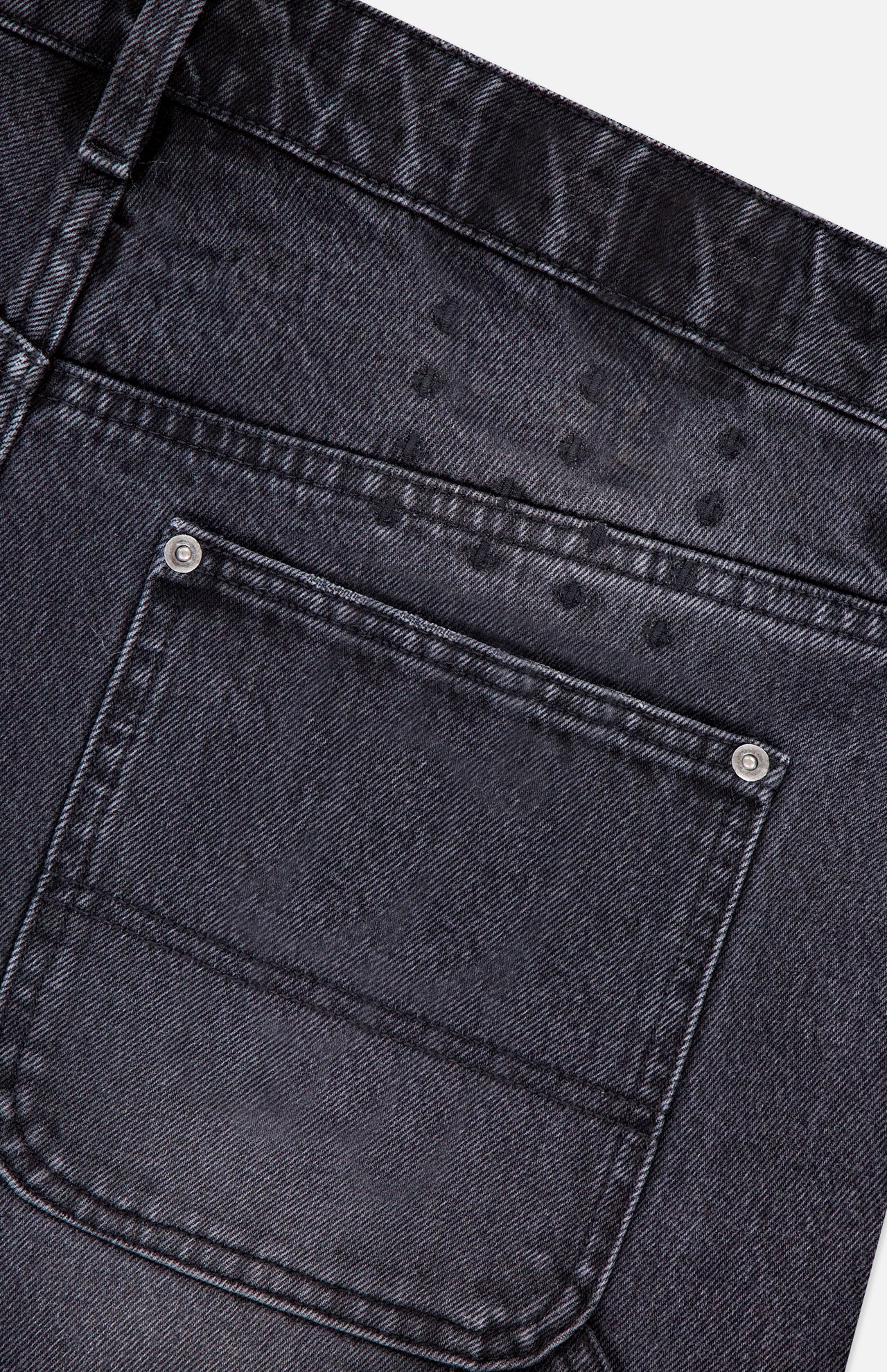 Close-up of the back carpenter pocket on KSUBI Maxx Operator Jean Shorts in black denim, featuring subtle water spots above the pocket and two metal rivets at the corners.