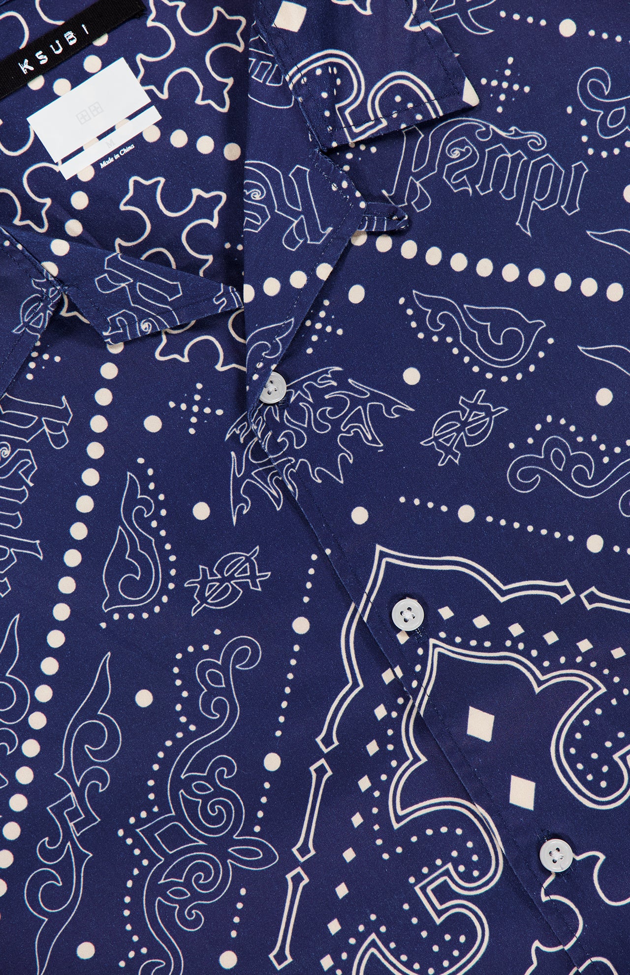 Close-up of the KSUBI Paise Diner Short Sleeve Shirt in navy blue, showcasing white paisley and geometric bandana prints, a Cuban collar with buttons, and a visible KSUBI label near the collar.