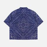 A navy short-sleeve Paise Diner Shirt by KSUBI, featuring a white paisley bandana print and a classic Cuban collar, displayed flat with the back side facing up.