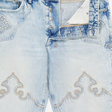 KSUBI Toro Western Knee Paneling Jeans in light blue feature a silver-toned button fly, intricate stitched patterns on the thighs and pocket area, and a slightly faded, distressed finish. The partially open fly reveals white pocket lining, while classic embroidered denim details lend a subtle western flair.