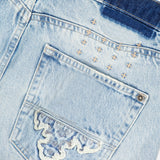 Close-up of the back pocket of the KSUBI Toro Western Knee Paneling Jeans in light blue denim, featuring decorative stitching, faded areas, and visible embroidered details above and on the pocket.
