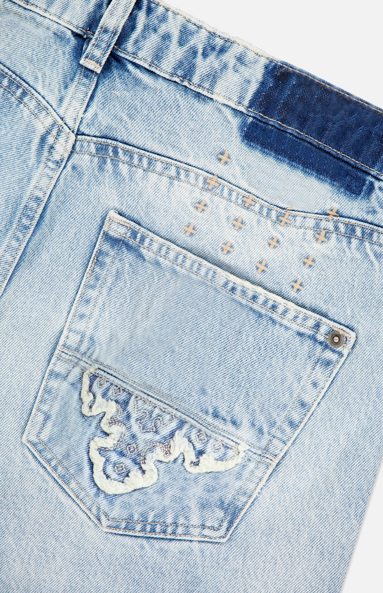 Close-up of the back pocket of the KSUBI Toro Western Knee Paneling Jeans in light blue denim, featuring decorative stitching, faded areas, and visible embroidered details above and on the pocket.