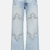 The KSUBI Toro Western Knee Paneling Jeans feature a light blue, wide-leg silhouette with decorative embroidered stitching on the front, showcasing curved designs above the knees and on the pockets for a vintage, faded look.