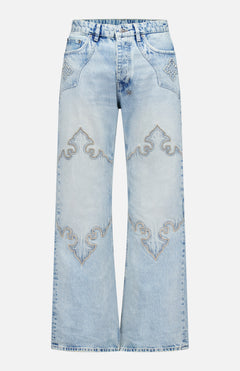 The KSUBI Toro Western Knee Paneling Jeans feature a light blue, wide-leg silhouette with decorative embroidered stitching on the front, showcasing curved designs above the knees and on the pockets for a vintage, faded look.