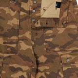 Close-up of the KSUBI Troop Camouflage Cargo Pant, crafted from durable cotton twill in brown and olive camo, featuring large front pockets, a partially open button fly, a visible waistband, and a metal D-ring detail on the left side.