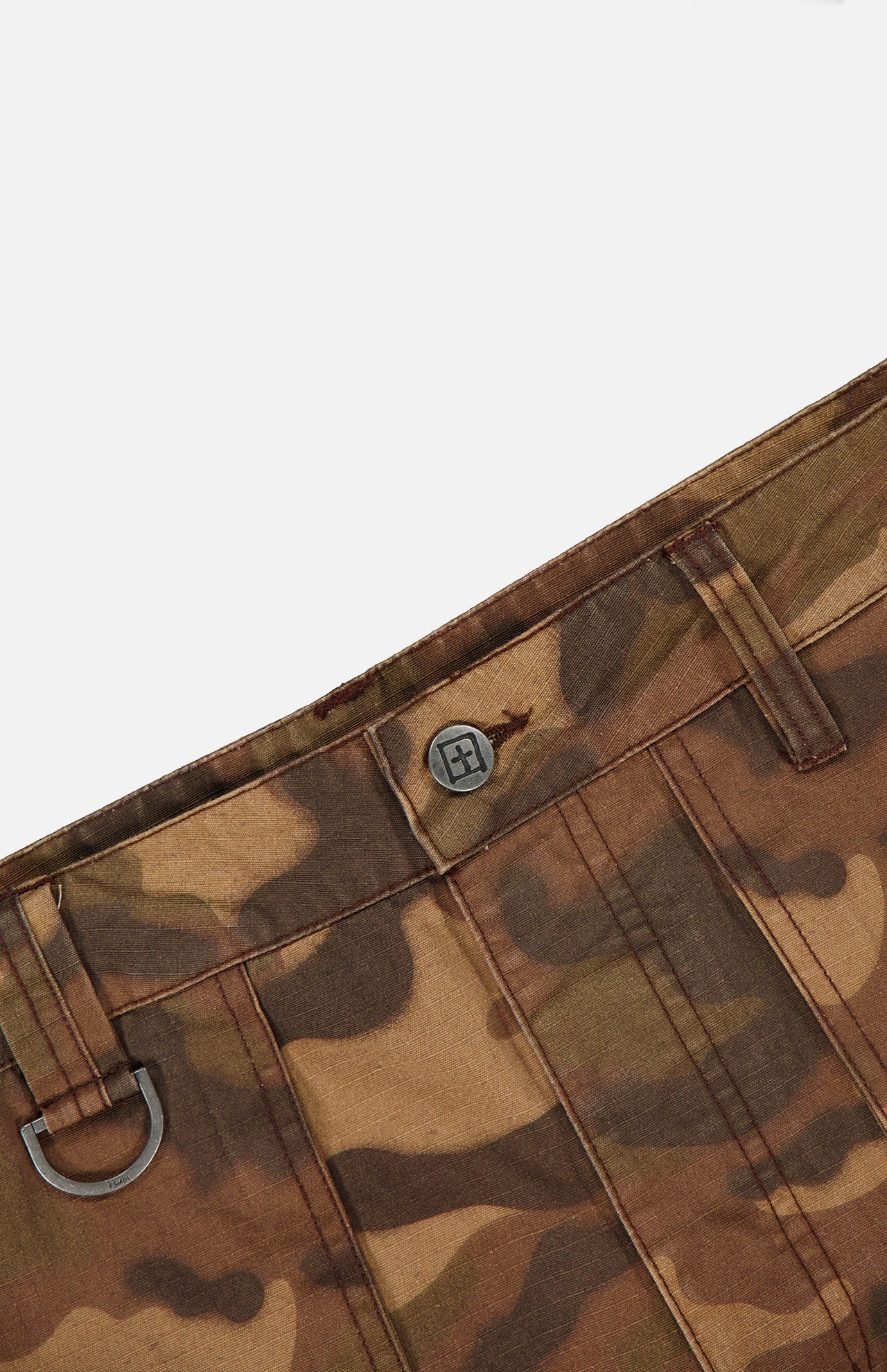 Close-up of the waistband of the KSUBI Troop Camouflage Cargo Pant, showcasing a branded button, belt loops, and a metal D-ring detail on one loop.