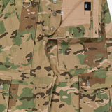 Close-up of the KSUBI Trooper Camouflage Cargo Pant featuring woodland camo, metal buttons, belt loops, multiple pockets, and a visible KSUBI patch above the left knee. The open fly reveals the inside label and relaxed leg fit.