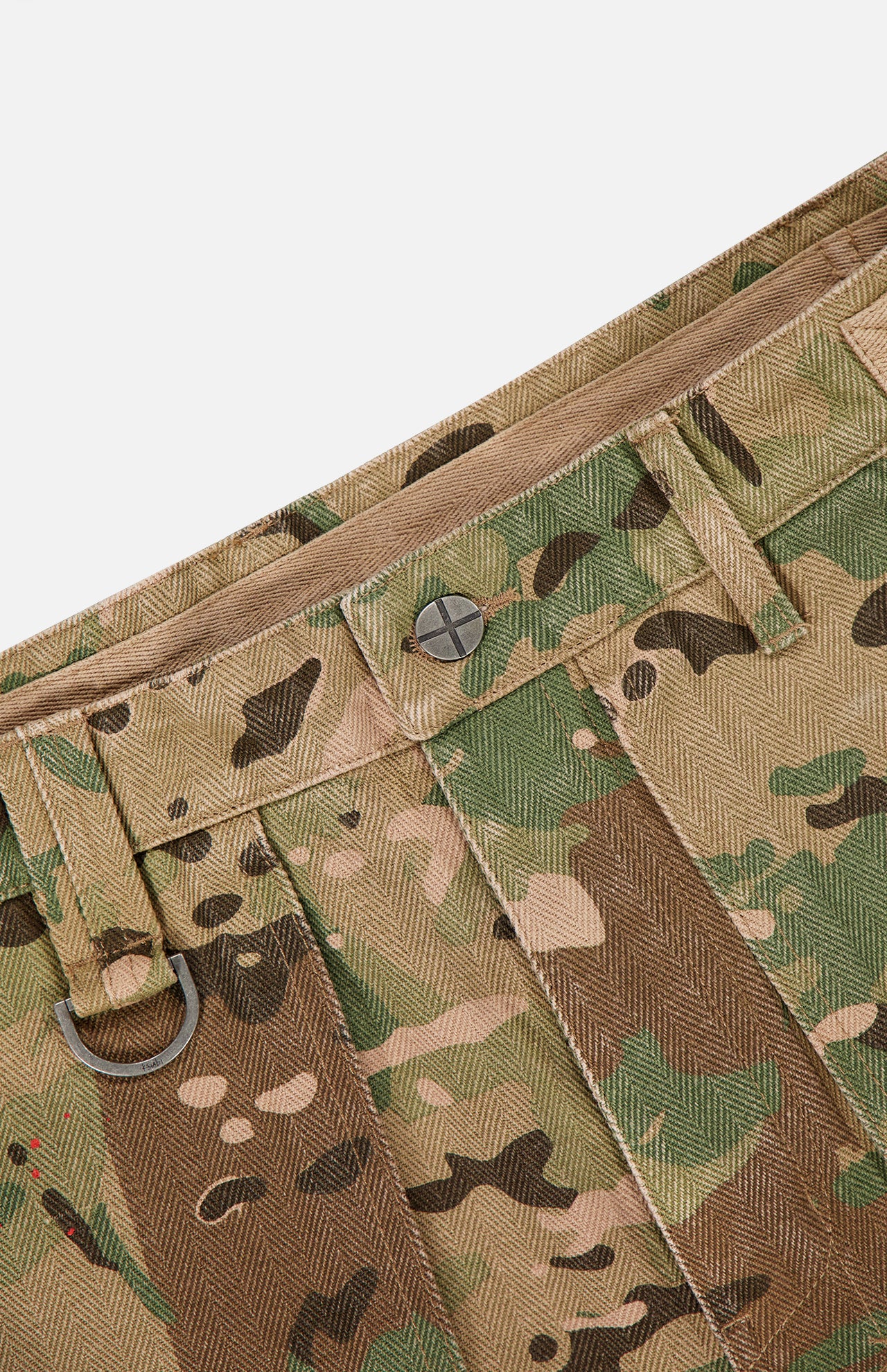 A close-up of the KSUBI Trooper Camouflage Cargo Pant waistband highlights woodland camo, a metal button, belt loops, a D-ring, and herringbone weave texture.