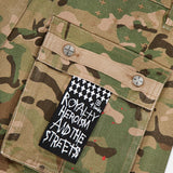 A close-up of the KSUBI Trooper Camouflage Cargo Pant pocket, featuring two metal rivets and a black and white label with "ROYALTY HEROISM AND THE STREETS" in bold, graffiti-style text.