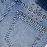 Close-up of the back pocket of KSUBI Van Winkle Duke 4Eva Jeans in light blue comfort stretch denim, showcasing brown stitching and small metallic pyramid studs arranged in a partial grid above the pocket. These skinny jeans offer a perfect balance of style and ease.