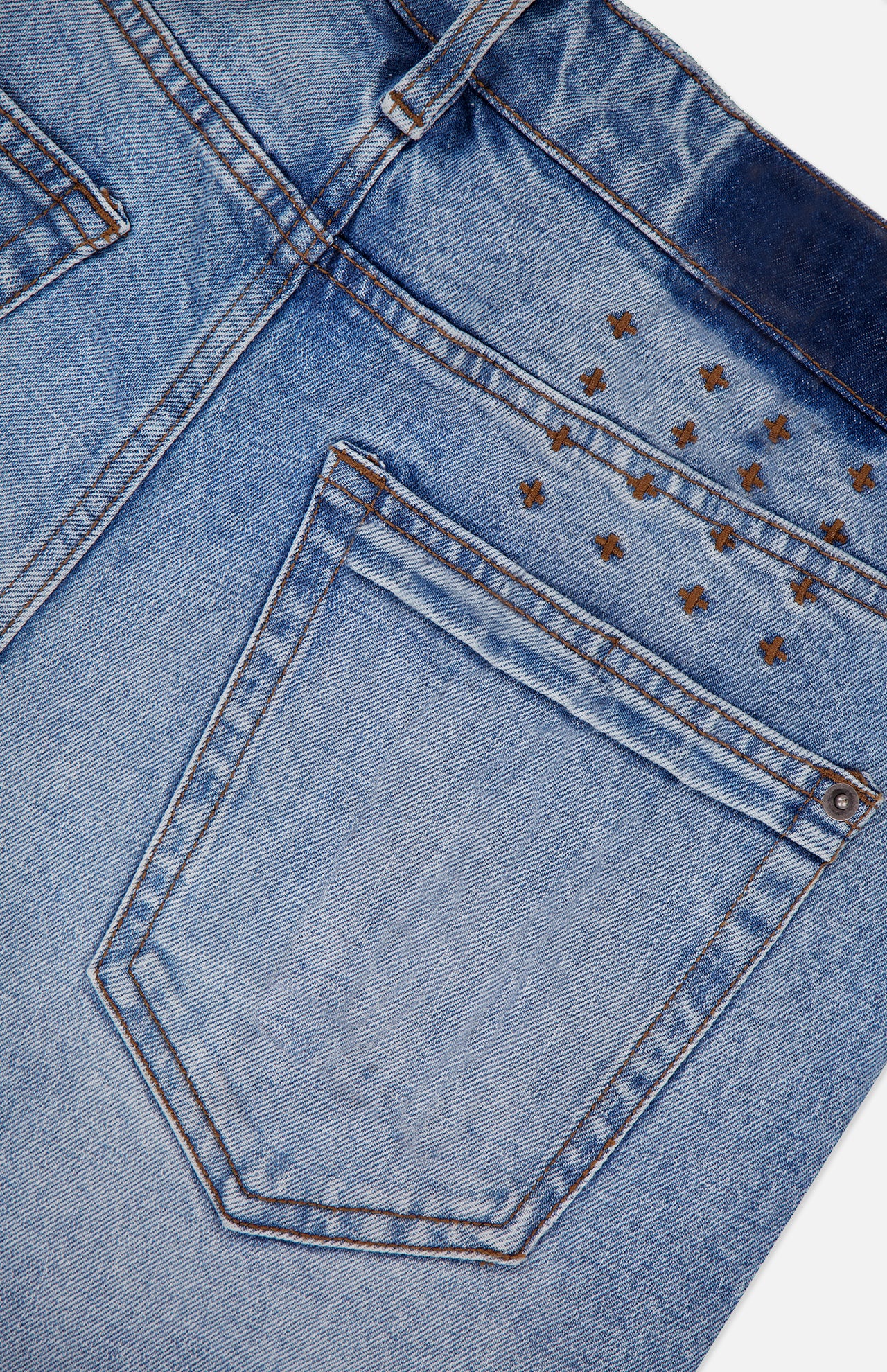 Close-up of the back pocket of KSUBI Van Winkle Duke 4Eva Jeans in light blue comfort stretch denim, showcasing brown stitching and small metallic pyramid studs arranged in a partial grid above the pocket. These skinny jeans offer a perfect balance of style and ease.