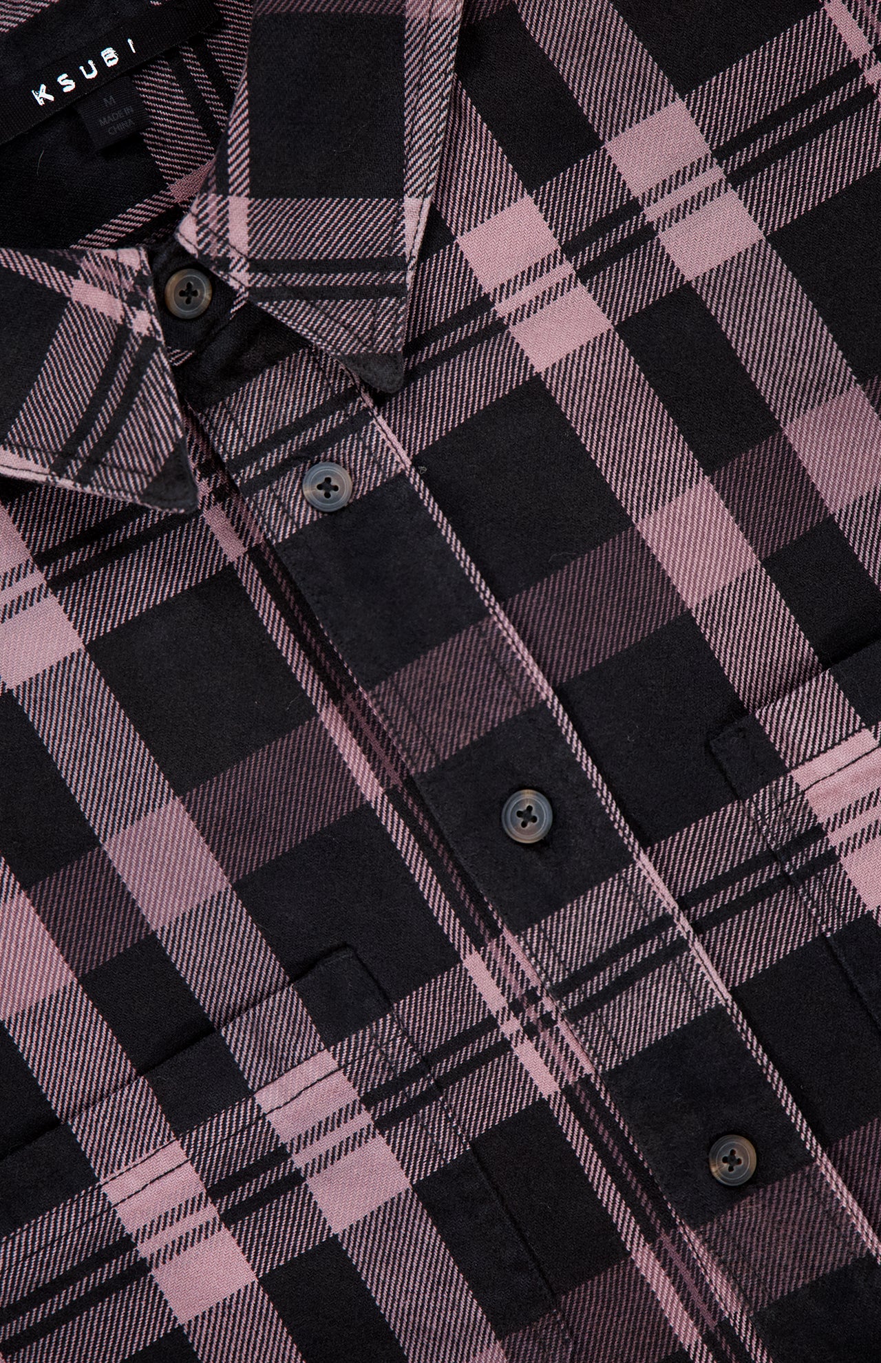 Close-up of the KSUBI Vulture Flannel Long Sleeve Shirt featuring a pink and black plaid pattern. Highlights include the collar, buttons, front pocket, and textured fabric with a checkered design.