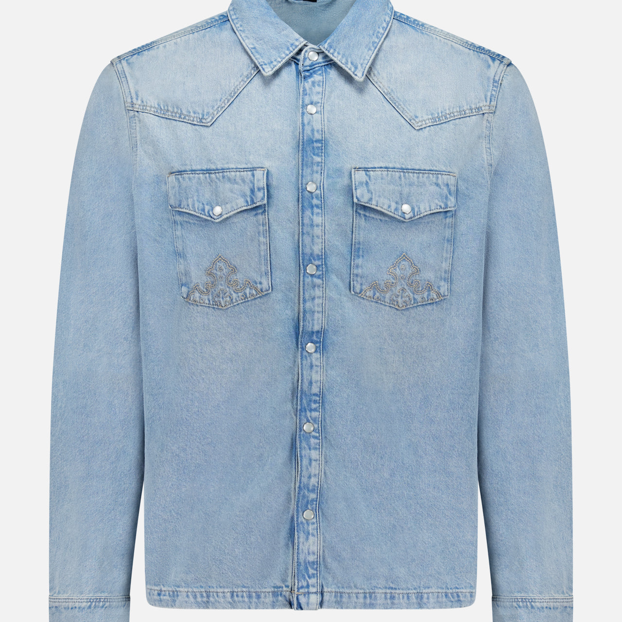 The Whiplash Long Sleeve Western Shirt by KSUBI features a light blue, slightly faded denim fabric, long sleeves, a pointed collar, button-down front, and two chest pockets with flap closures. Its casual finish gives this classic western shirt a relaxed yet timeless appeal.