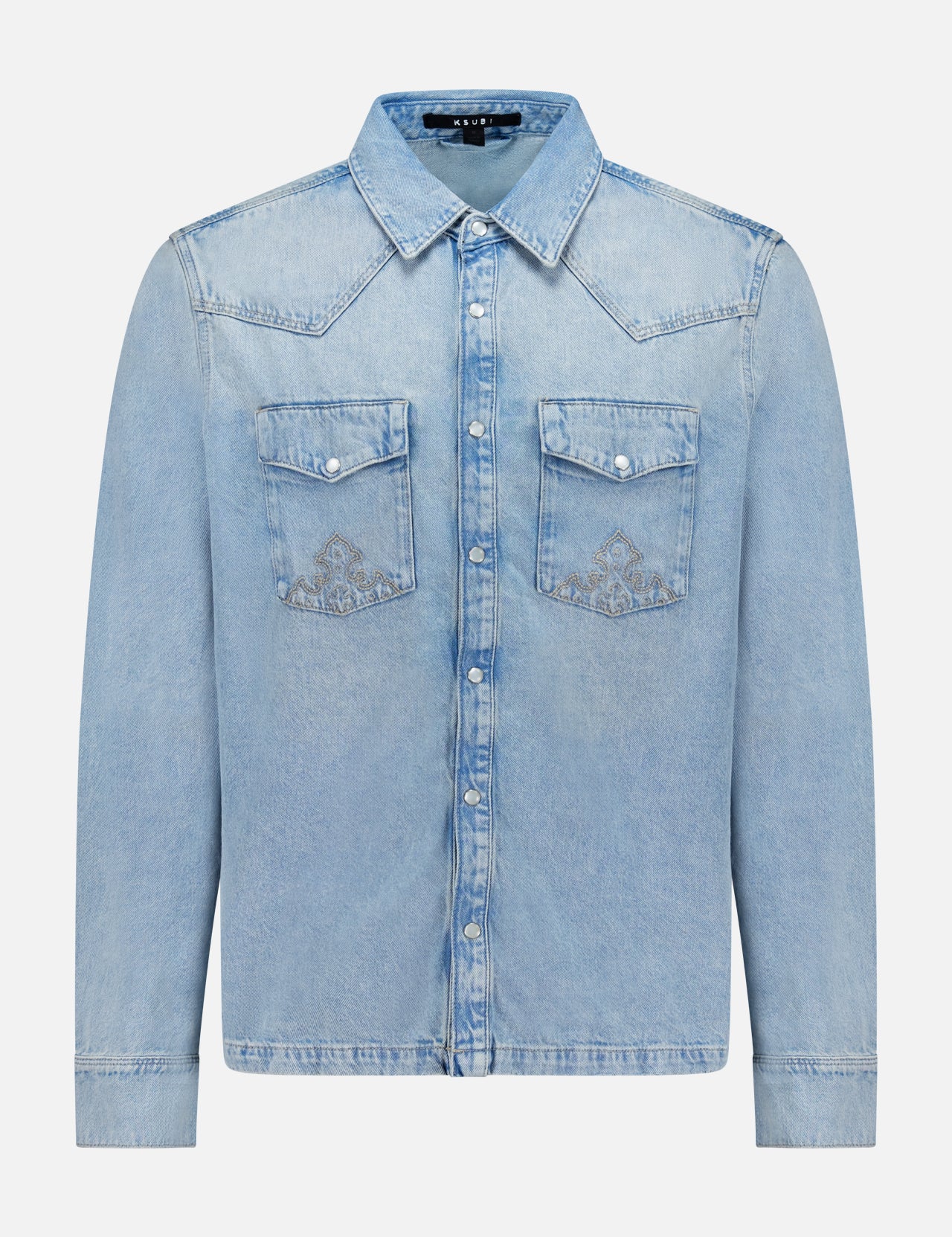 The Whiplash Long Sleeve Western Shirt by KSUBI features a light blue, slightly faded denim fabric, long sleeves, a pointed collar, button-down front, and two chest pockets with flap closures. Its casual finish gives this classic western shirt a relaxed yet timeless appeal.