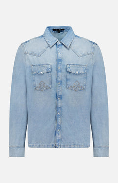 The Whiplash Long Sleeve Western Shirt by KSUBI features a light blue, slightly faded denim fabric, long sleeves, a pointed collar, button-down front, and two chest pockets with flap closures. Its casual finish gives this classic western shirt a relaxed yet timeless appeal.