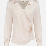 The Bernice Satin Wrap Blouse by L'AGENCE is a pale beige champagne long-sleeve top with a V-neckline, wrap design, fabric buttons on the chest, and softly gathered shoulders finished with elegant cuffs.