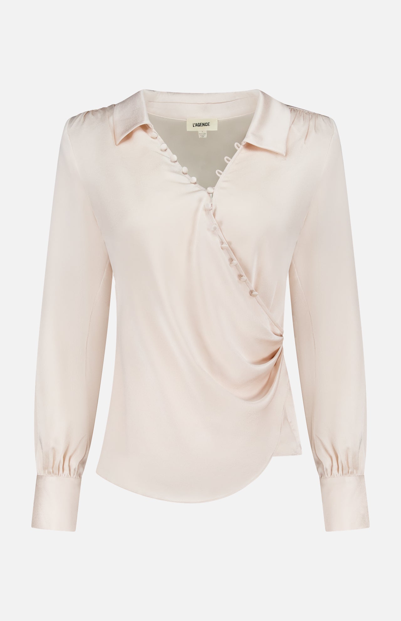 The Bernice Satin Wrap Blouse by L'AGENCE is a pale beige champagne long-sleeve top with a V-neckline, wrap design, fabric buttons on the chest, and softly gathered shoulders finished with elegant cuffs.
