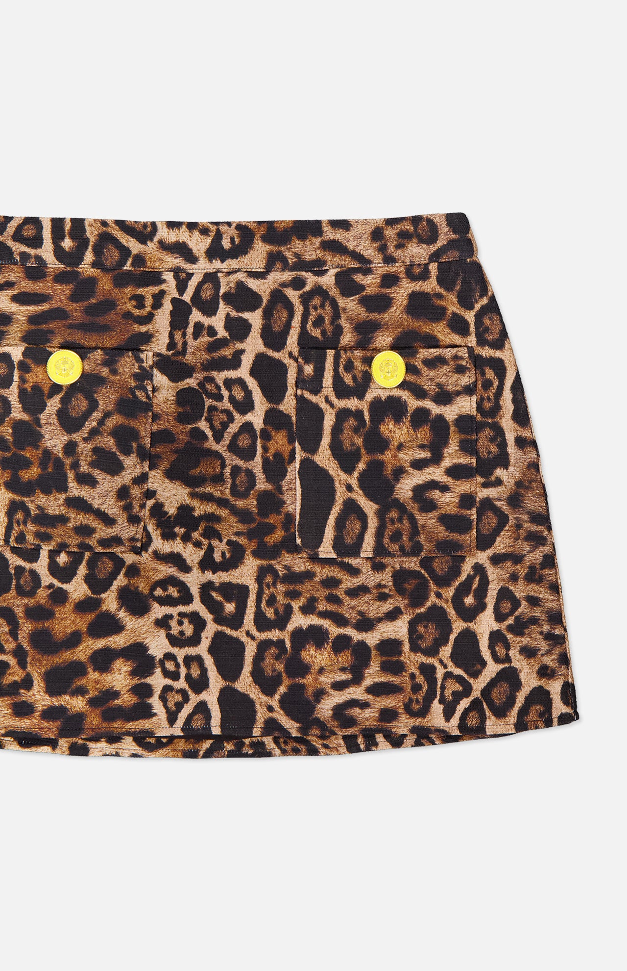 A close-up of the Cyra Low Rise Mini Skirt by L'AGENCE, showcasing a leopard print pattern with two front pockets, each adorned with a round yellow button, set against a white background.
