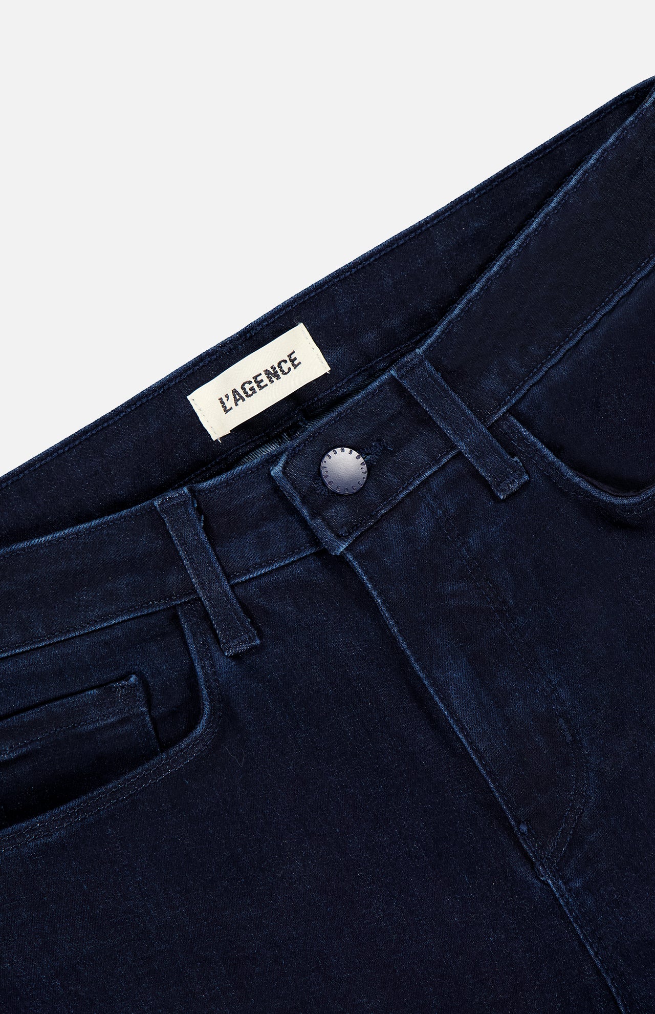 Close-up of the waistband and front pockets of the Marguerite High Rise Skinny Jean by L’Agence, in dark blue stretch denim with a silver button and visible inner brand label, combining comfort and style.
