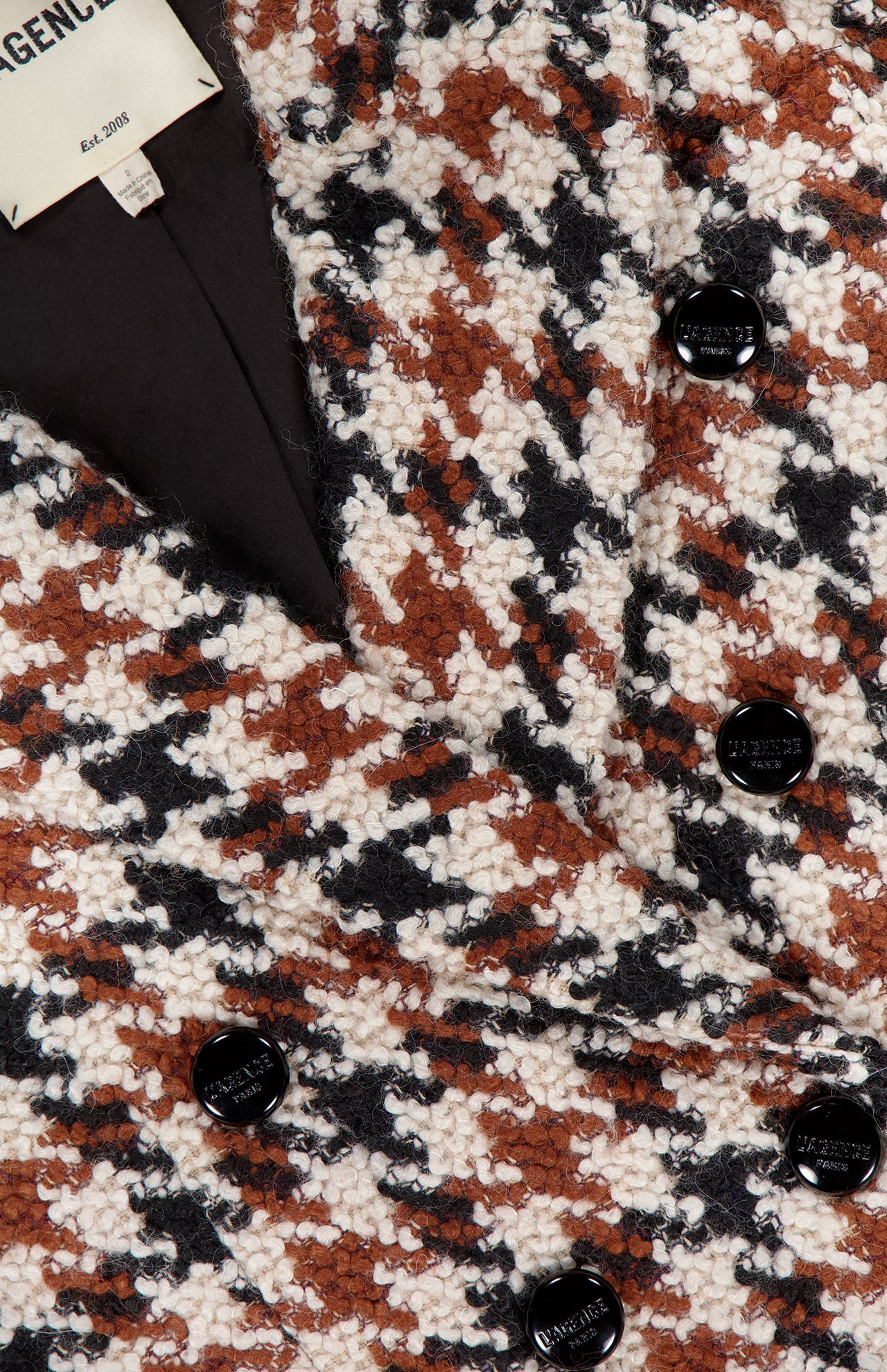 Close-up of L'AGENCE Marie Double Breasted Houndstooth Blazer in brown, black, and white boucle with black buttons and a visible label—ideal for a cinched-waist tweed look.
