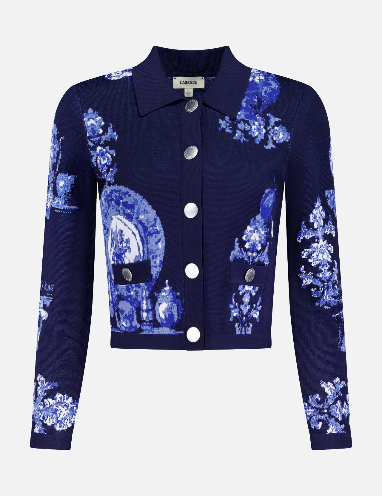The Osiris Jacquard Collared Cardigan by L'AGENCE is a navy blue, long-sleeve cropped statement piece with silver buttons and a pixelated blue and white porcelain motif of plates, vases, and florals.