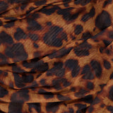 A close-up of L'AGENCE's Rasha Shirred Tank Top shows stretch mesh fabric with a leopard print—dark brown and black spots on light brown—gathered to suggest a shirred waist and a semi-sheer, stylish look.