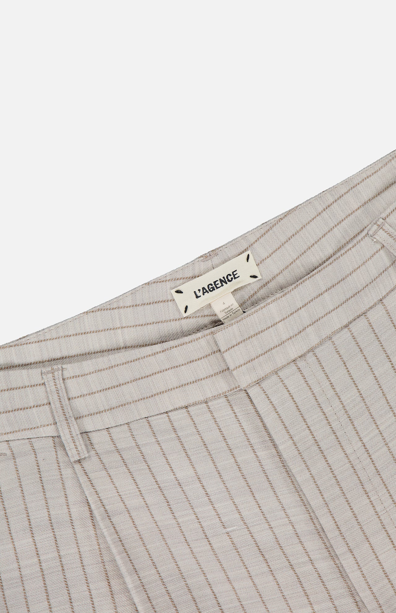 Close-up of the waistband and label of the Allanah Mid Rise Trouser Pant in tan pinstripe. The L’AGENCE label is sewn inside, emphasizing these timeless pants.