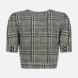 The Allegra Short Sleeve Cropped Jacket by L’AGENCE, shown from the back against a white background, features a black and white plaid pattern with gold buttons on the short sleeves, offering a timeless take on the classic cropped tweed jacket.
