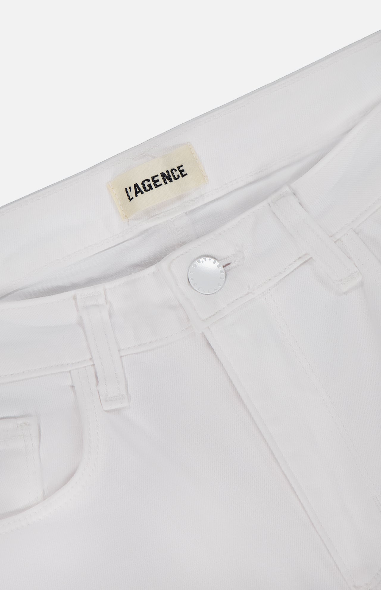 Close-up of the waistband and front pocket of Amaris High Rise Skinny Pedal Pusher Pants in white, featuring a silver button and an inner label that reads L'AGENCE.