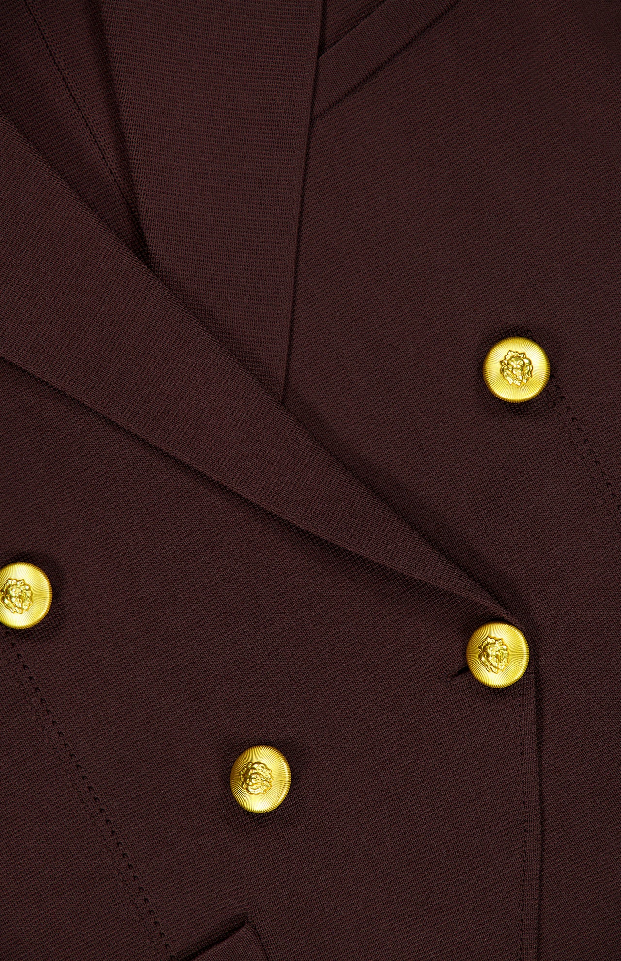 Close-up of the Amelia Knit Blazer by L’AGENCE, a dark brown tailored piece accented with shiny gold engraved buttons. The fabric texture and detailed button design are clearly visible.