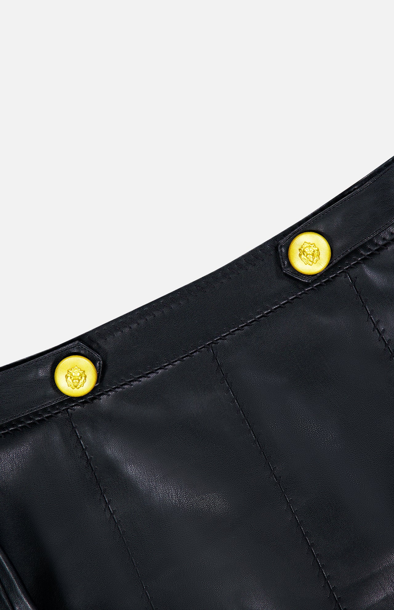 Close-up of the Arlena Whipstitch Mini Skirt by L’AGENCE, crafted from sleek black leather with visible whipstitch detailing and finished with two shiny gold embossed buttons, set against a plain light background.