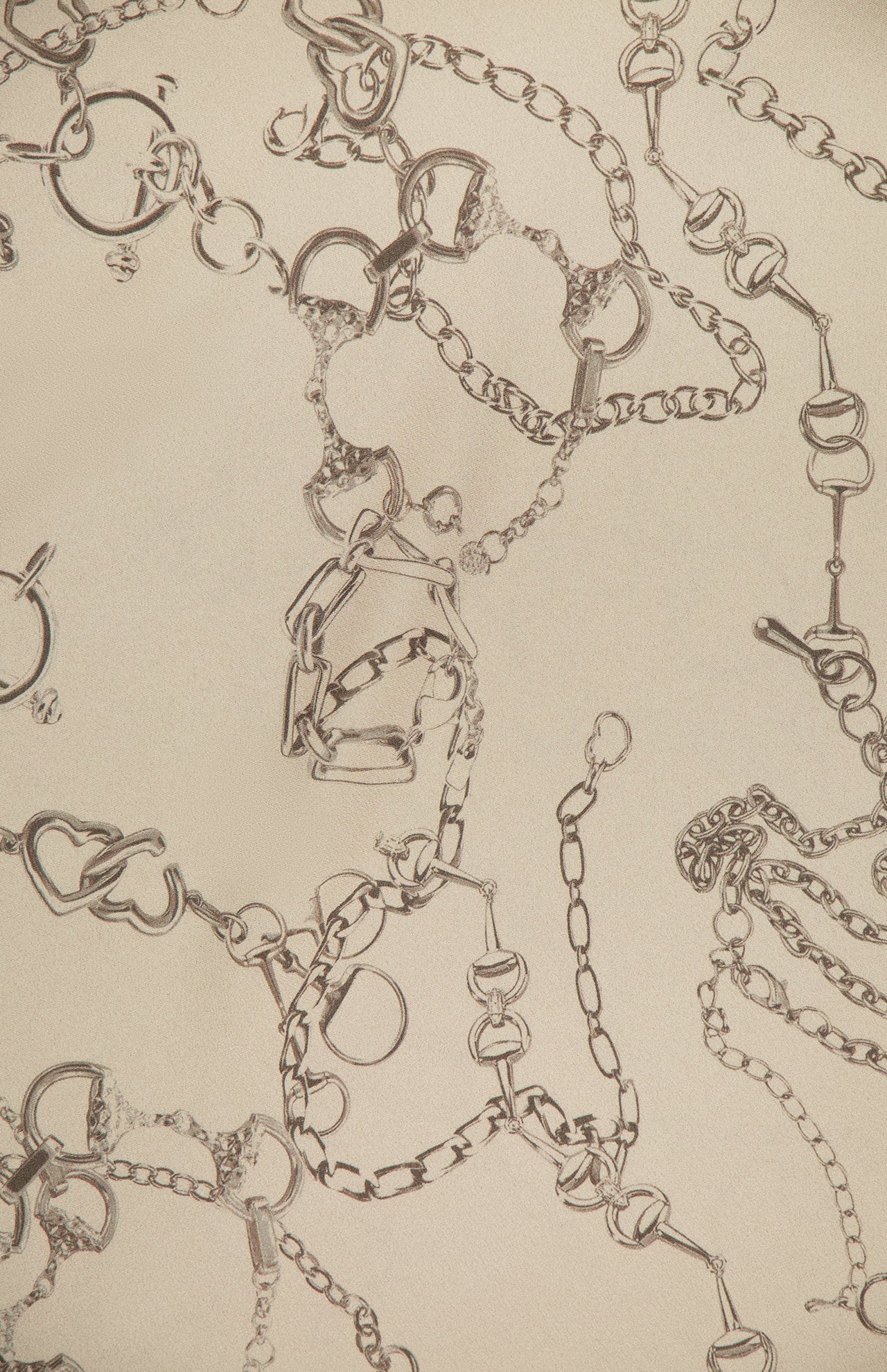 Metallic heart and circle link jewelry is scattered over a beige background, reflecting the elegant chain motif of the Asami Chain One Shoulder Blouse by L'AGENCE.