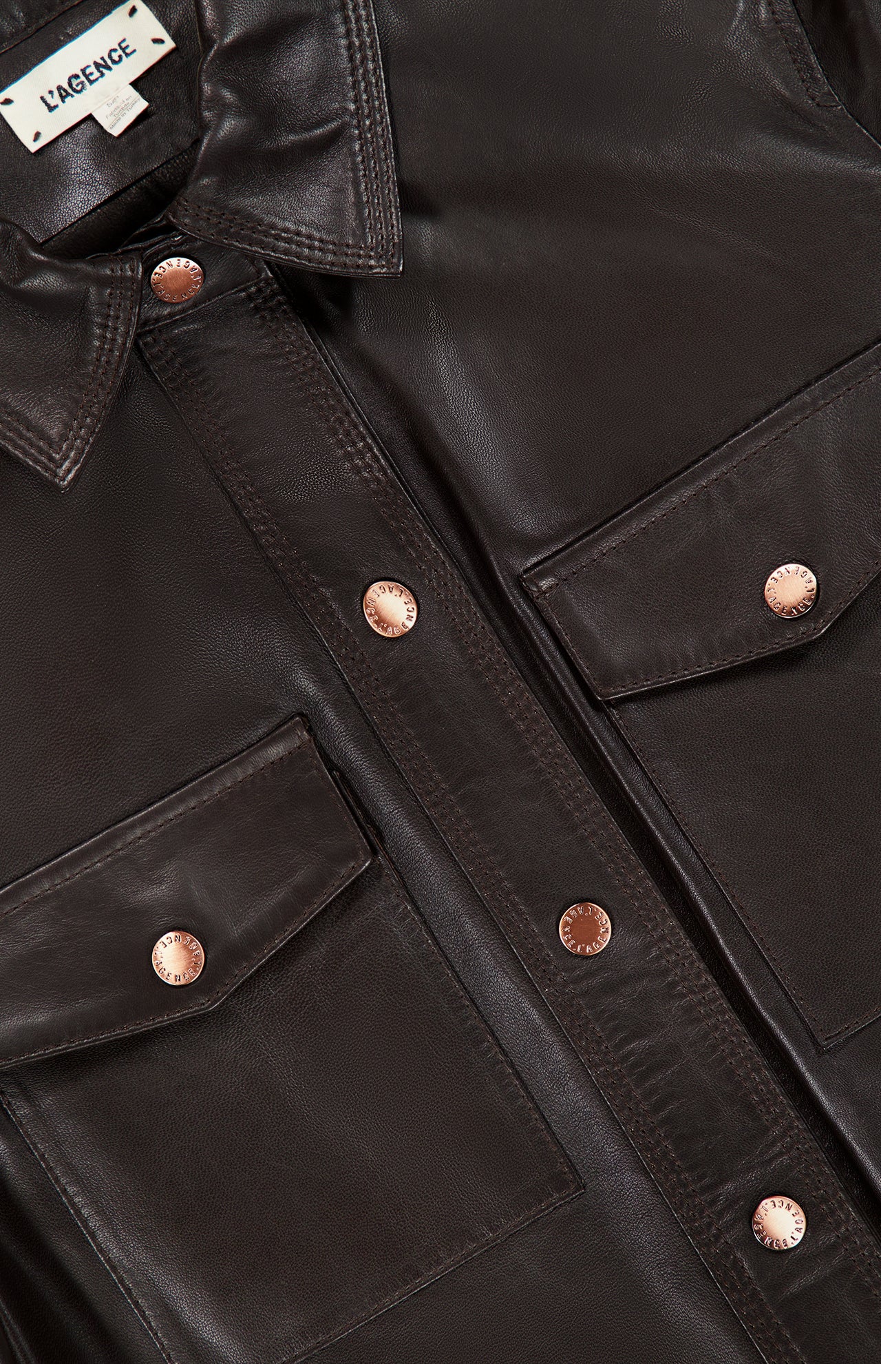 Close-up of the Avina Leather 3/4 Sleeve Blouse by L’AGENCE in dark brown lamb leather, featuring two front pockets, copper-colored buttons, and a visible L’AGENCE label on the collar.