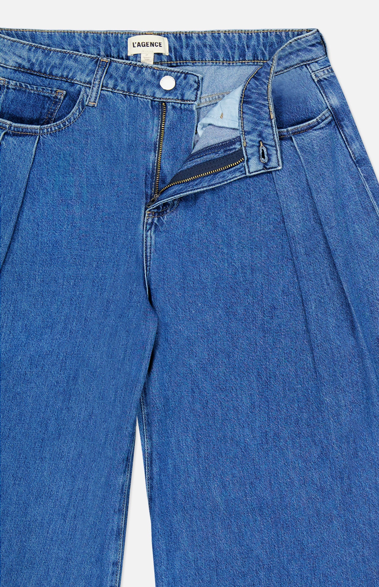 A pair of Chayse High Rise Super Wide Leg Jeans in Towson by L’AGENCE, featuring blue denim with a partially unzipped fly and open button that reveals the inner waistband and signature brand tag.