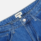 Close-up of the Chayse High Rise Super Wide Leg Jean in Towson, featuring blue denim with a front button closure, belt loops, and visible stitching. A white label with the brand name L’AGENCE is sewn inside the waistband.