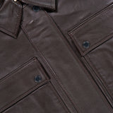 Close-up of the Clotilde Leather Bomber Jacket by L’AGENCE in dark brown, featuring two front flap pockets, black snap buttons, and a visible L’AGENCE label inside the collar.