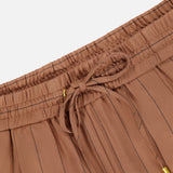 Close-up of the Connie Drawstring Pinstripe Trouser by L'AGENCE in brown with thin black pinstripes, featuring wide legs, a pleated design, an elastic waistband, and a drawstring tied in a bow with gold metal tips.