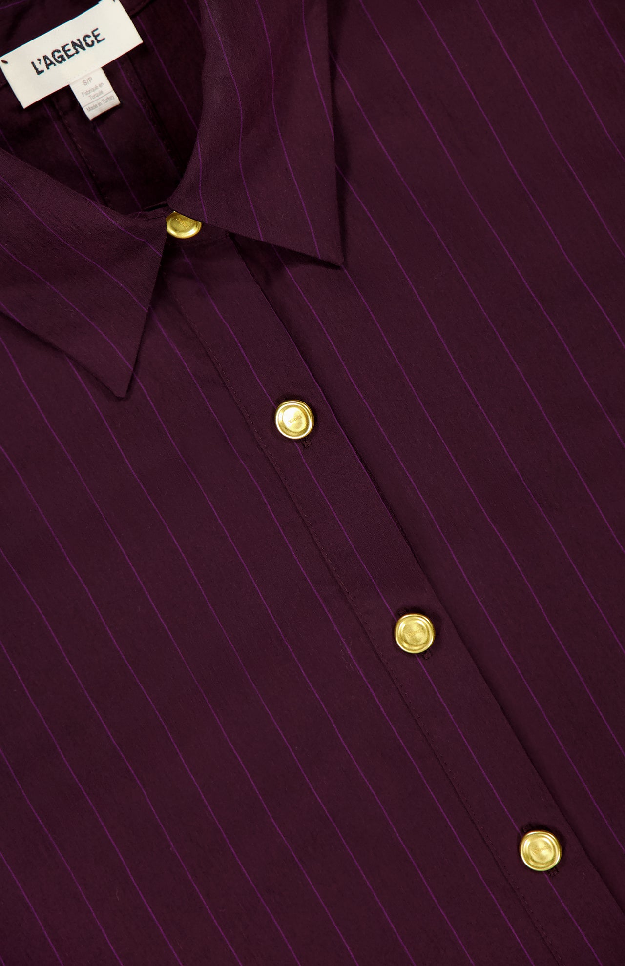 Close-up of the L’AGENCE Cosette Crop Hi Low Shirt, featuring deep purple and burgundy pinstripes, gold-tone coin buttons, a pointed collar, and a modern cropped high-low hem.