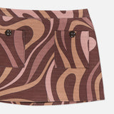 A close-up of the L'AGENCE Cyra Low Rise Mini Skirt showcases its brown and pink abstract swirl print, two front pockets each fastened with a black button, and an eye-catching low-rise silhouette.