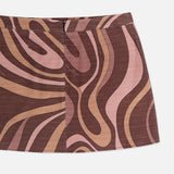 The Cyra Low Rise Mini Skirt by L'AGENCE is showcased against a white background. This mini skirt features a bold, abstract swirl print in wavy brown, pink, and beige patterns. It has a low rise fit with a fitted waistband and a center seam for added detail.