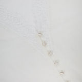 A close-up of the Eluna Lace Detail Cardigan by L'AGENCE, featuring an off-white hue with a lace pattern and a row of small cowrie shells for a delicate, elegant look.
